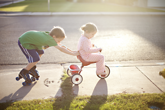 Some acts of kindness for kids can nurture your family's bond, like this brother helping to push his little sister on her tricycle