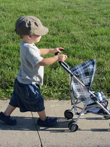 A boy pushing a baby doll in a stroller