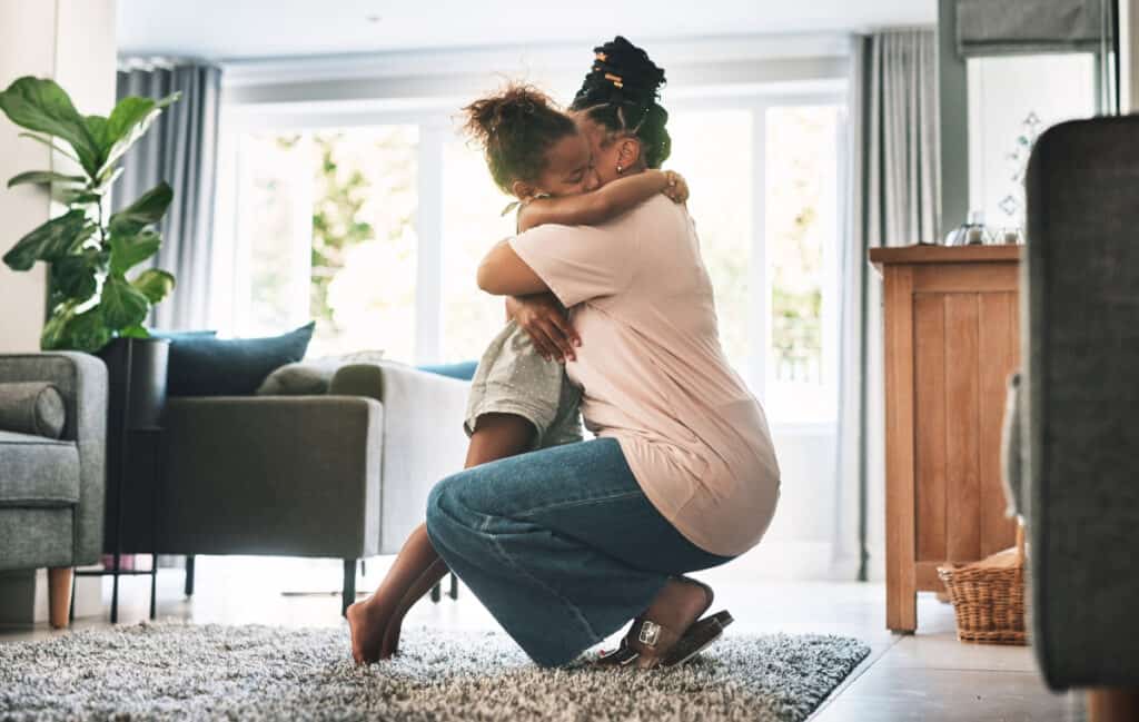 The answer to how to hug a child? With your whole heart. (Pictured: A mom bends down to hug her daughter, and her daughter's arms are around the mother's neck.)